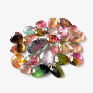 May include: A collection of multi-colored, faceted, gemstone beads. The beads are various shades of pink, green, yellow, and black. The beads are oval shaped and have a smooth, polished finish.