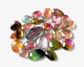 Può includere: Una collezione di perline di pietre preziose sfaccettate multicolori. Le perline sono di varie tonalità di rosa, verde, giallo e nero. Le perline sono di forma ovale e hanno una finitura liscia e lucida.