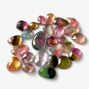 May include: A collection of 20 faceted, multi-colored gemstones. The stones are various shades of pink, green, yellow, and brown. The stones are all cut in a teardrop shape.