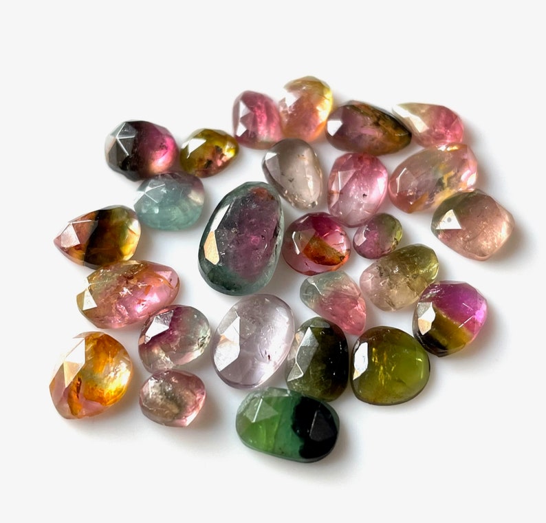 May include: A collection of 20 faceted, multi-colored gemstones. The stones are various shades of pink, green, yellow, and brown. The stones are all cut in a teardrop shape.