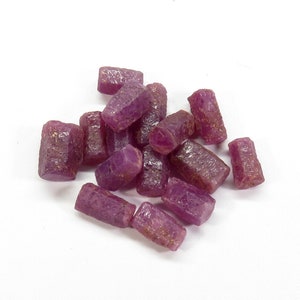 Op de afbeelding: Een groep kleine, ruwe, roze robijnkristallen. De kristallen zijn gefacetteerd en hebben een natuurlijke, ruwe uitstraling.