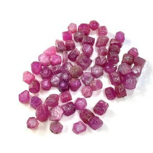 Op de afbeelding: Een verzameling kleine, roze robijn edelstenen. De robijnen zijn gefacetteerd en hebben verschillende vormen en maten.