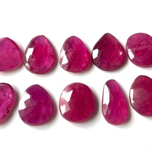 Può includere: Dieci pietre preziose di rubino sfaccettate a forma di lacrima. Le pietre preziose sono di colore rosa intenso e hanno una finitura lucida.