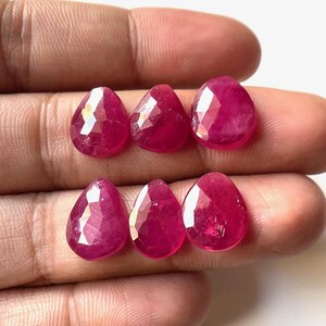 May include: Six faceted ruby gemstone drops in a teardrop shape. The gemstones are a deep red color and have a glossy finish.