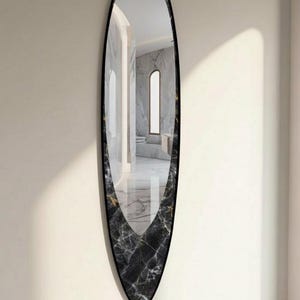 Puede incluir: Espejo ovalado con marco negro y un patrón similar al mármol en la base. El espejo refleja una habitación con suelo de mármol. El diseño es moderno y elegante, adecuado para un interior contemporáneo. El espejo mide aproximadamente 180 cm de altura.