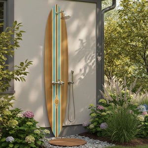 Pode incluir: Chuveiro exterior com design de prancha de surf. A prancha de surf de madeira tem listras azul claro e marrom escuro. O chuveiro e os acessórios são prateados. Um tapete circular de madeira fica sobre um leito de seixos. Plantas e flores verdes circundam o chuveiro.