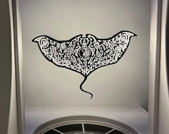 May include: A black and white decorative stingray wall art piece. The stingray features intricate tribal patterns and designs. The art is mounted on a white ceiling, with a curved window and architectural details visible below.