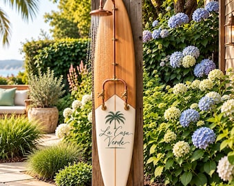 May include: An outdoor shower fixture mounted on a wooden surfboard. The surfboard features a light wood top and a white bottom with a palm tree graphic and the text La Casa Verde. A copper shower head and pipes are attached to the board.