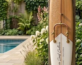 May include: An outdoor shower mounted on a surfboard with a light wood top and white bottom. The copper plumbing features a round shower head and two brass handles. The surfboard displays the text California Surf Culture Dana Point California.