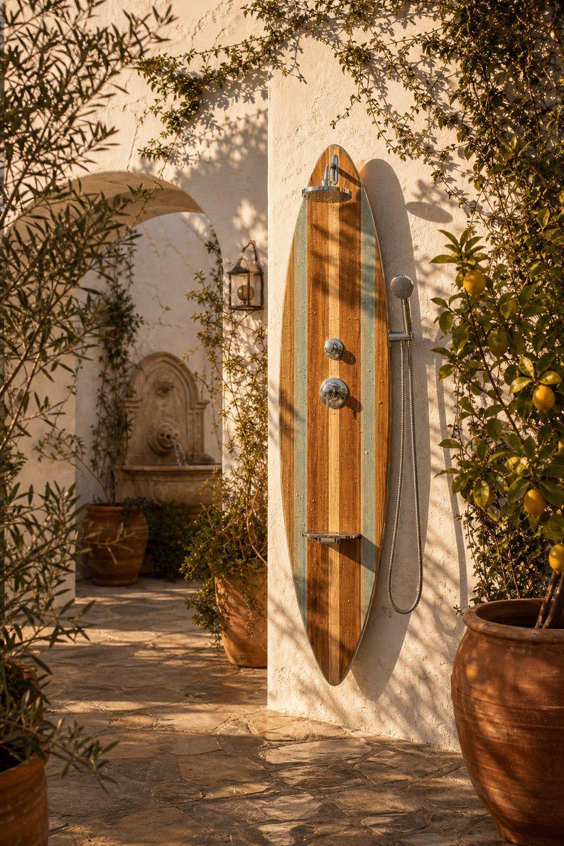 May include: An outdoor shower panel shaped like a surfboard, featuring vertical wood grain stripes in natural brown and light blue. It includes a chrome overhead shower head, a central control valve, a small metal shelf, and a handheld shower sprayer.