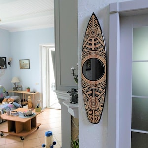 May include: A decorative surfboard-shaped mirror with a black border and intricate geometric patterns in light brown. The mirror is mounted on a white wall, adding a unique touch to the interior decor.