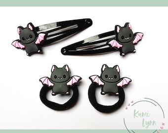Può includere: Set di quattro accessori per capelli a forma di pipistrello nero. Due fermagli per capelli neri con ciondoli a forma di pipistrello rosa e due elastici per capelli neri con ciondoli a forma di pipistrello rosa.