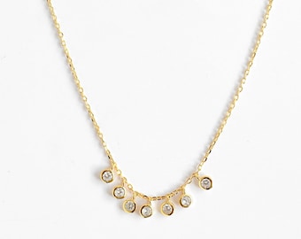 May include: A delicate gold necklace with a series of small, round, clear gemstones dangling from the chain. The necklace is displayed against a white background, highlighting the jewelry's design and sparkle.