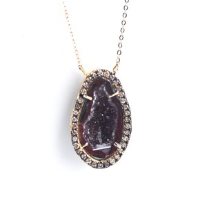 Puede incluir: Un collar de cadena de oro con un colgante que presenta una geoda de ágata marrón rodeada por un halo de pequeños diamantes.
