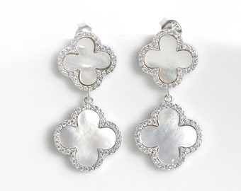 May include: A pair of silver earrings with a double clover design. Each clover is adorned with a white mother-of-pearl center and a sparkling clear crystal border.
