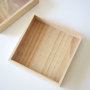 May include: Two wooden trays, one is larger than the other. Both trays are made of light brown wood with a natural finish. The trays are empty and have a square shape.