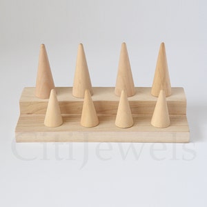 May include: Wooden ring display stand with eight cone-shaped ring holders. The stand is made of light brown wood and has two levels.