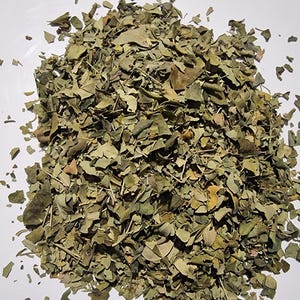 May include: A pile of dried, crushed green leaves with varying shades of olive and brown. The texture is brittle and fragmented, consisting of small, irregular leaf pieces and thin, woody stems scattered across the central area of the frame.