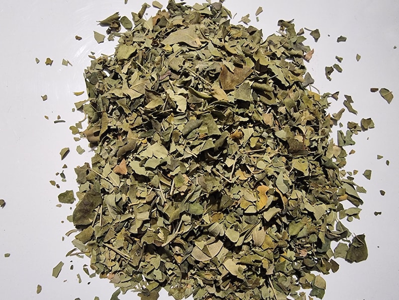 May include: A pile of dried, crushed green leaves with varying shades of olive and brown. The texture is brittle and fragmented, consisting of small, irregular leaf pieces and thin, woody stems scattered across the central area of the frame.