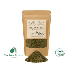May include: A brown paper pouch containing dried spearmint leaves, with a clear window showing the green contents. The label reads SPEARMINT LEAF (Mentha spicata) above a mountain graphic and the website www.treeoflove.shop, with a 100% natural logo.