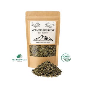 Può includere: Una busta in carta kraft marrone contenente una miscela di tè con una finestra trasparente che mostra erbe verdi essiccate e bacche scure. L'etichetta riporta la scritta MORNING SUNSHINE TEA BLEND con un grafico di montagna e il sito www.treeoflove.shop.