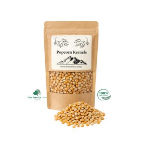 Könnte beinhalten: Ein brauner Papierbeutel gefüllt mit gelben Popcorn-Maiskörnern. Das Etikett zeigt eine Berggrafik, den Text Popcorn Kernels und www.treeoflove.shop. Ein Haufen loser gelber Maiskörner liegt vor dem Beutel.