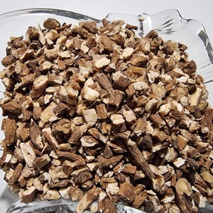 May include: A clear glass bowl filled with a large quantity of dried, chopped brown root pieces. The pieces vary in size and shape, displaying a mix of dark brown bark-like exteriors and lighter, cream-colored fibrous interiors throughout the pile.
