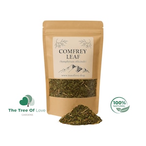 May include: A brown paper pouch containing dried comfrey leaf, labeled with the text COMFREY LEAF (Symphytum officinale) and www.treeoflove.shop. A small pile of the green dried leaves sits in front of the pouch, which features a clear window.