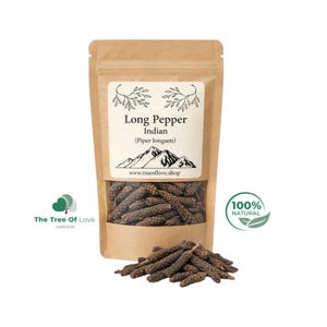 Può includere: Una busta in carta kraft marrone contenente pepe lungo indiano, etichettata con il testo Long Pepper Indian (Piper longum) e un grafico di montagna. Un piccolo mucchio di grani di pepe scuri, strutturati e cilindrici si trova davanti.
