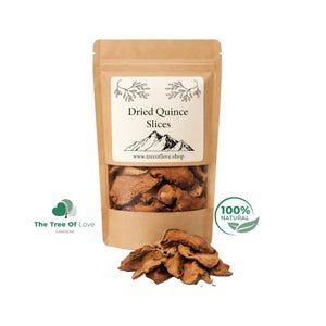 Puede incluir: Una bolsa de papel marrón con rodajas de membrillo seco. La etiqueta muestra el texto Dried Quince Slices, un gráfico de montaña y el sitio web www.treeoflove.shop. Un montón de rodajas de membrillo seco se encuentra frente a la bolsa.
