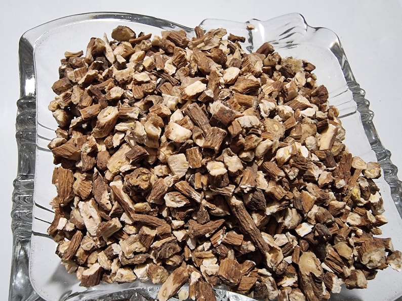 May include: A clear glass bowl filled with a large quantity of dried, chopped brown root pieces. The pieces vary in size and shape, displaying a mix of dark brown bark-like exteriors and lighter, cream-colored fibrous interiors throughout the pile.