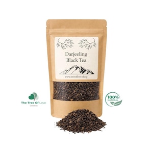 Może przedstawiać: Brązowa torebka z papieru pakowego zawierająca czarną herbatę Darjeeling z białą etykietą z grafiką gór i napisem 'Darjeeling Black Tea' oraz 'www.treeoflove.shop'. Przed torebką znajduje się stos luźnych, ciemnych liści herbaty.