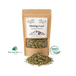 May include: A brown kraft paper stand-up pouch containing dried Moringa Leaf (Moringa Oleifera). The label features a mountain graphic, the text "Moringa Leaf (Moringa Oleifera)" and "www.treeoflove.shop". A pile of dried green leaves sits in front.