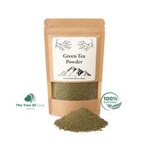 May include: A brown kraft paper pouch containing green tea powder with a clear window showing the contents. The label features the text Green Tea Powder, a mountain illustration, and the website www.treeoflove.shop. A pile of green tea powder sits in front.