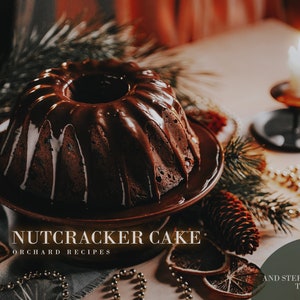 May include: A chocolate cake with a chocolate glaze and white drizzle, on a brown cake stand. The cake is surrounded by pine branches, gold beads, and dried orange slices. The text "NUTCRACKER CAKE" and "ORCHARD RECIPES" is displayed below the cake. The text "PDF RECIPE AND STEP BY STEP TUTORIAL" is displayed in the lower right corner of the image.