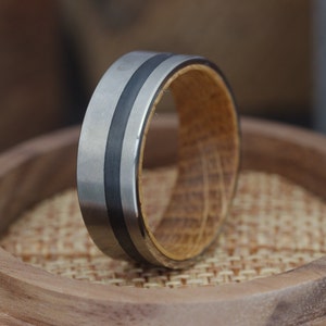 May include: A silver and black ring with a wood inlay. The ring is on a wooden surface.