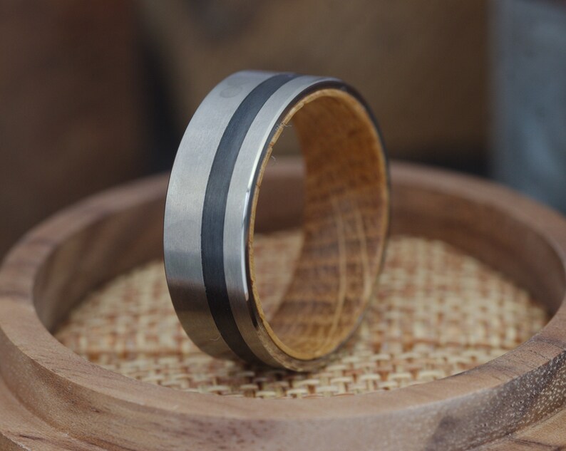 May include: A silver and black ring with a wood inlay. The ring is on a wooden surface.