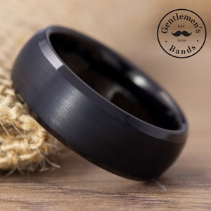 May include: A black tungsten carbide ring with a brushed finish. The ring has a beveled edge and is approximately 8mm wide.
