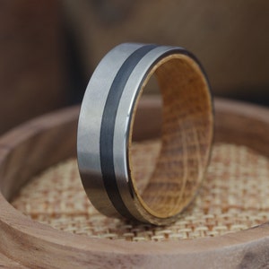 Op de afbeelding: Een zilveren en zwarte ring met een houten inlay. De ring ligt op een houten oppervlak.