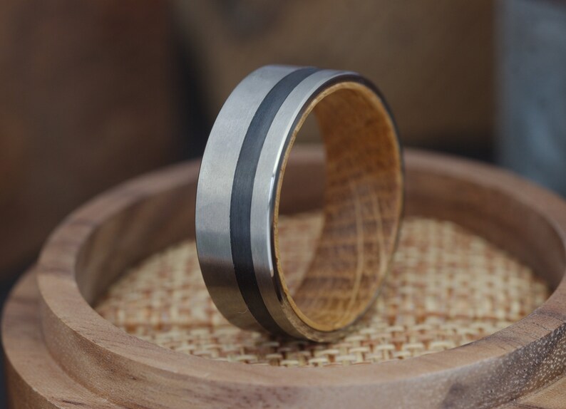 Op de afbeelding: Een zilveren en zwarte ring met een houten inlay. De ring ligt op een houten oppervlak.