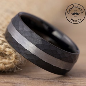 May include: A black tungsten carbide ring with a hammered finish and a silver inlay. The ring is on a burlap background.