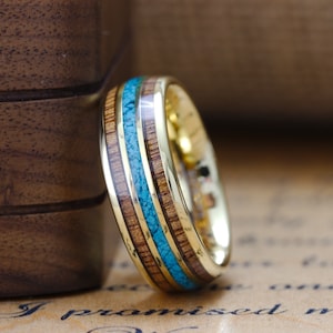 May include: A gold ring with a band of wood and turquoise inlay. The ring is on a piece of paper with the text "I promised my l" visible.
