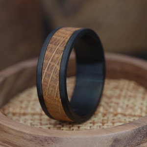 Op de afbeelding: Een zwarte en bruine ring met een houten inlay. De ring is gemaakt van een duurzaam materiaal en heeft een strak ontwerp.