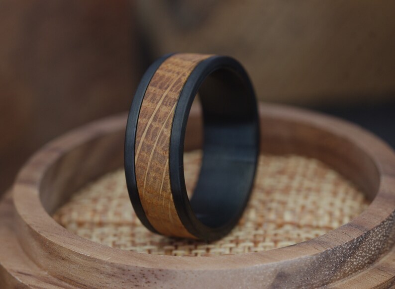 Op de afbeelding: Een zwarte en bruine ring met een houten inlay. De ring is gemaakt van een duurzaam materiaal en heeft een strak ontwerp.