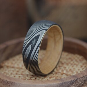 May include: A black and silver patterned ring with a wooden band. The ring is sitting on a wooden surface.