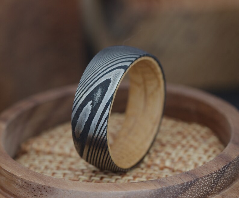 May include: A black and silver patterned ring with a wooden band. The ring is sitting on a wooden surface.