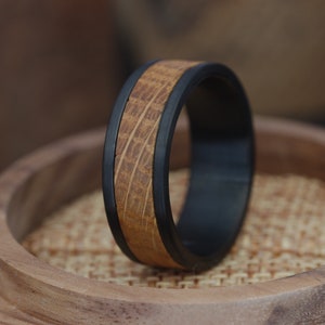 May include: A black and brown wooden ring with a wood grain pattern. The ring is on a wooden surface.