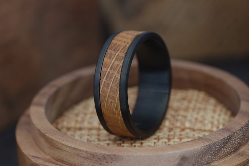 May include: A black and brown wooden ring with a wood grain pattern. The ring is on a wooden surface.