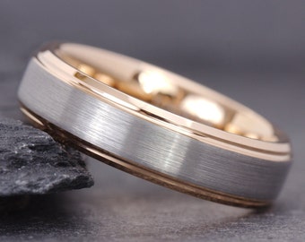 May include: A silver and rose gold wedding band with a brushed finish. The band has a thin rose gold trim around the edge.