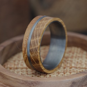 May include: A wooden ring with a silver band. The wood is a light brown colour and has a natural grain pattern. The ring is sitting on a wooden surface.